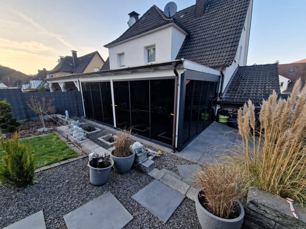 Terrassenüberdachung aus Aluminium in der Abenddämmerung mit Bepflanzung